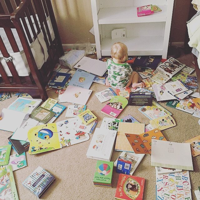 A baby on the floor surrounded by books scattered everywhere 