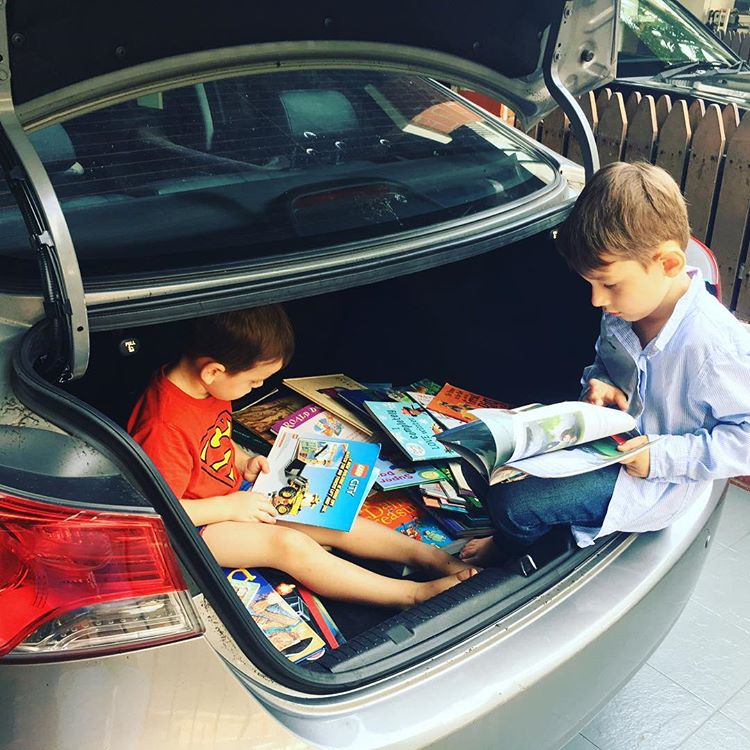 Two children in an open car boot with lots of books 