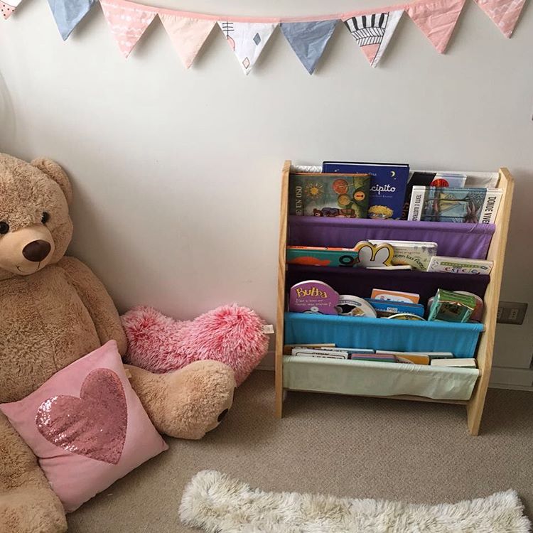 Huge teddy bear and cushions near a bookshelf 