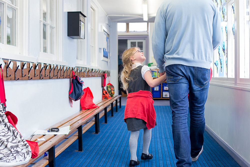 A photo of a dad walking his daughter down a school corridor on her first day