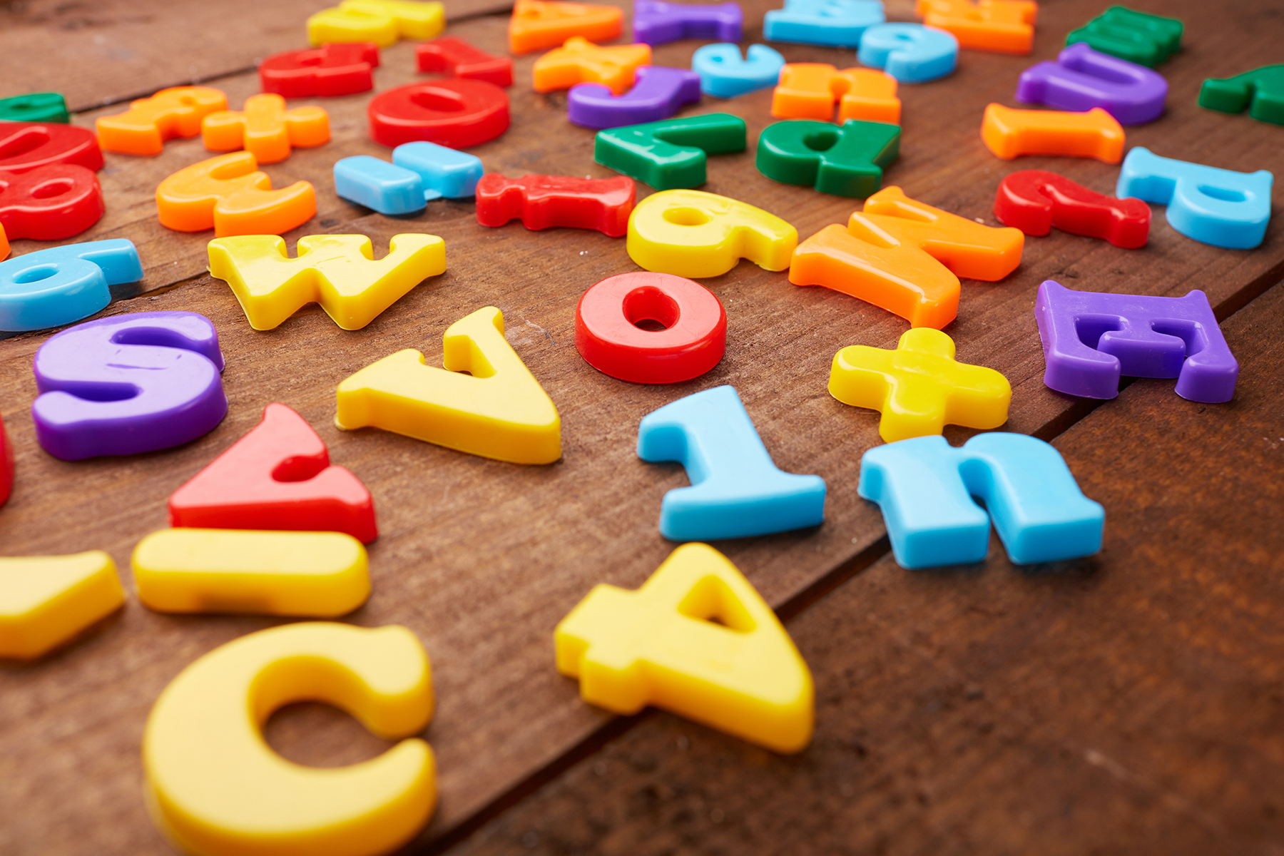 A photo of multicoloured magnetic letters and some numbers on a wooden table