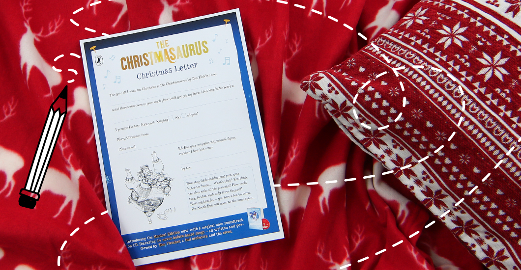 A photo of The Christmasaurus Christmas letter on a red blanket with a white reindeer design and a red fairisle cushion