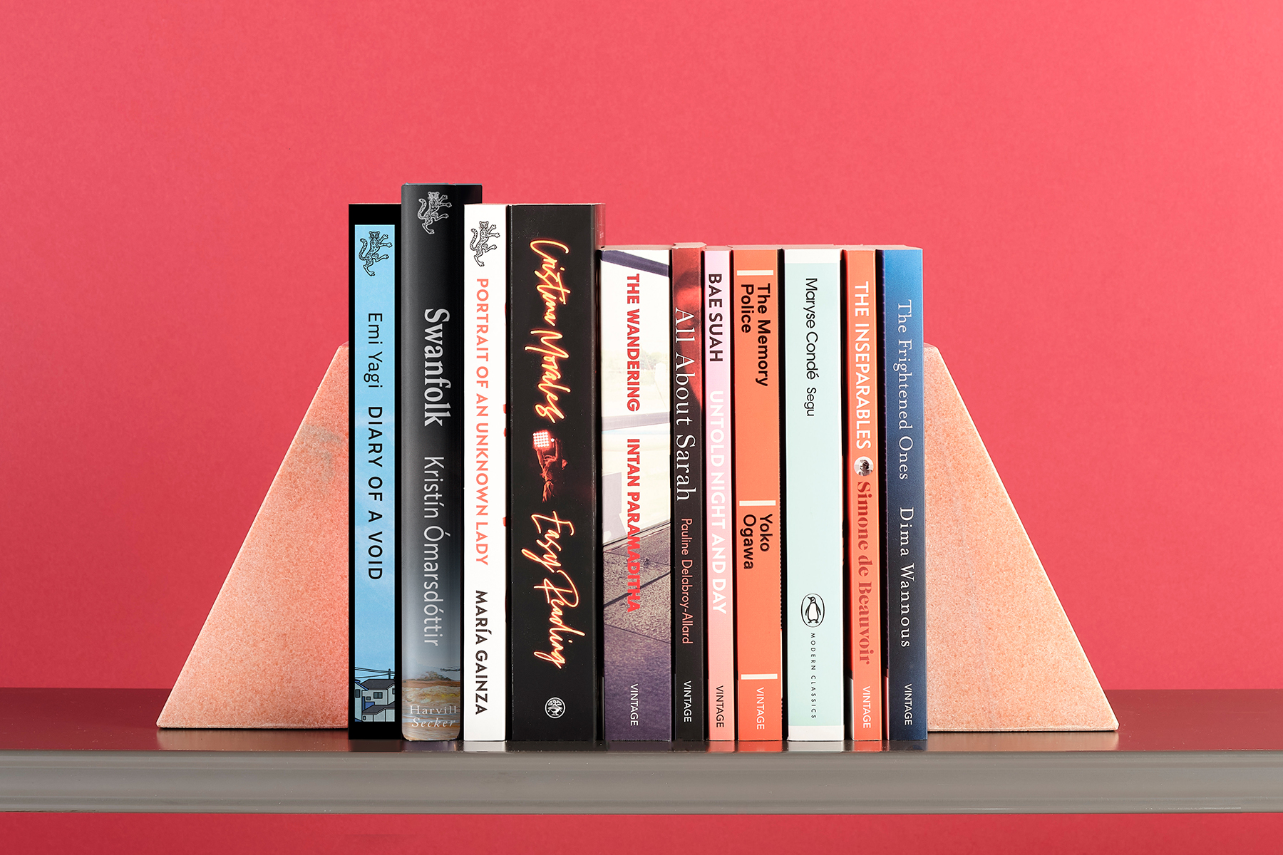 11 books by women in translation, lined up on a shelf to show spines, against a red background
