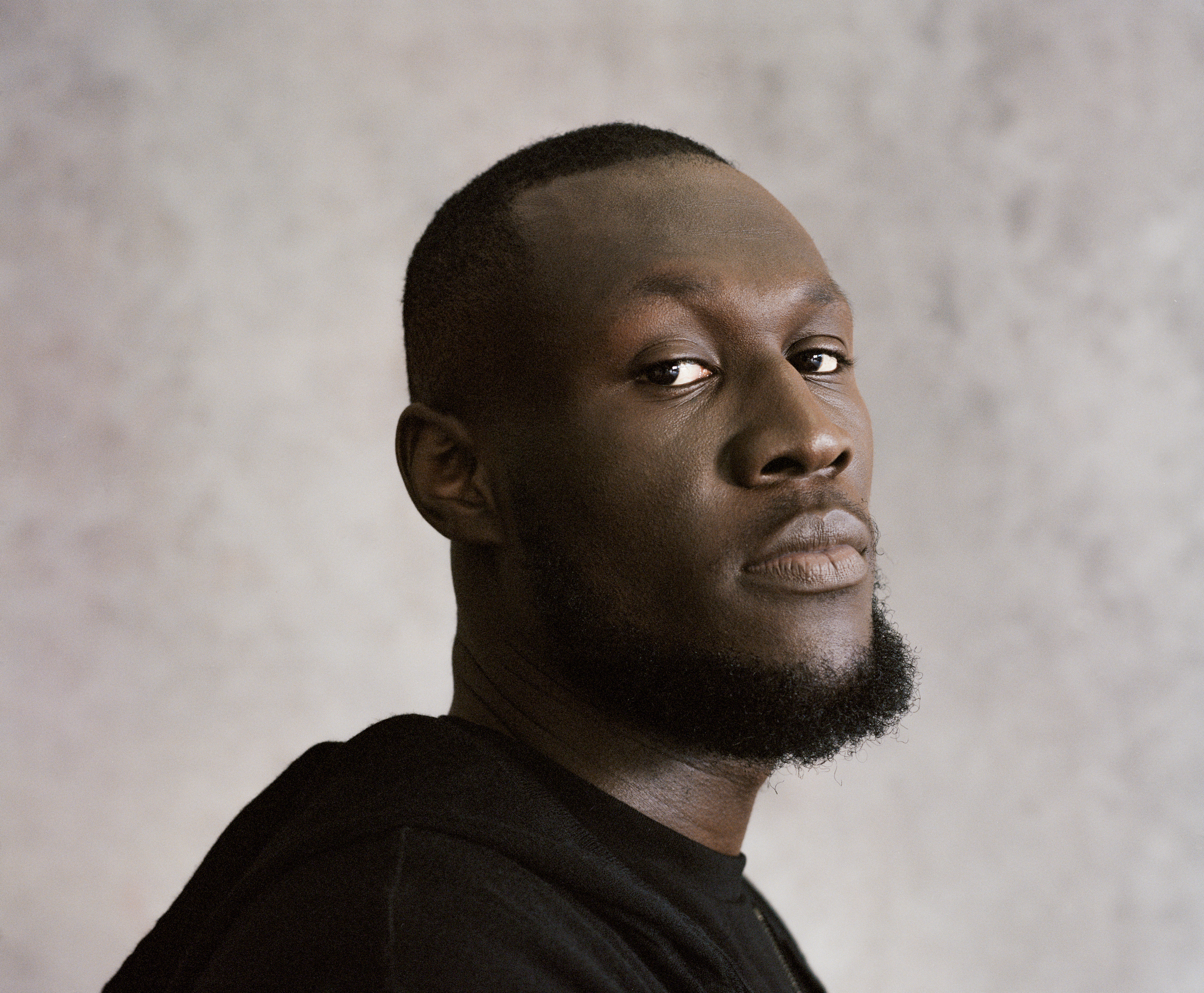 Head and shoulders picture of Stormzy, wearing a black t-shirt and top.