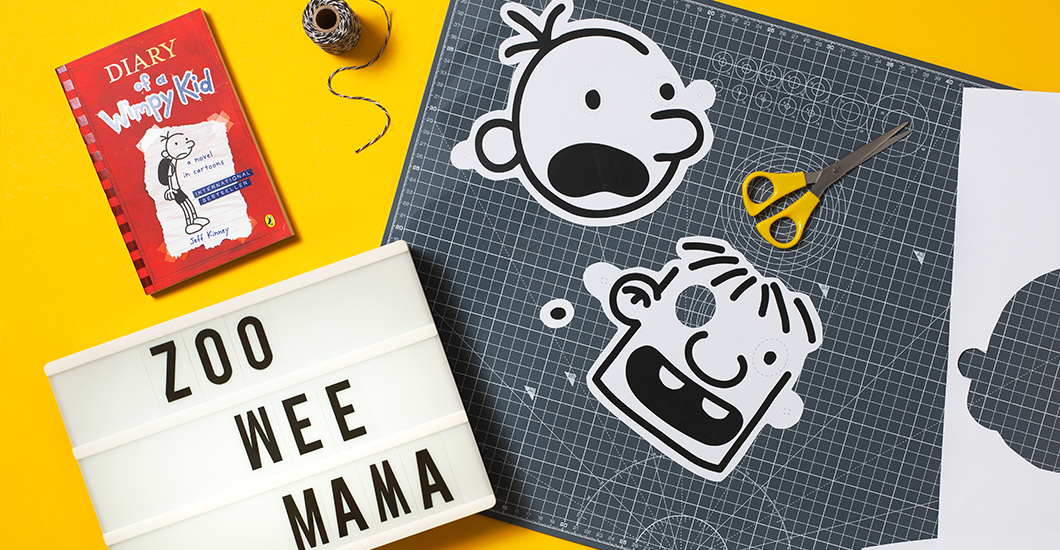 A photo of cut out masks of Greg Heffley and Rowley Jefferson on a yellow background next to some scissors and a copy of the book Diary of a Wimpy Kid