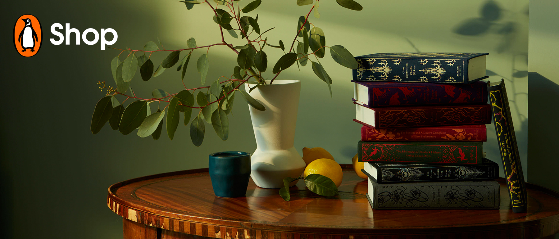 A stack of Clothbound Classics on bedside table with vase and lemon