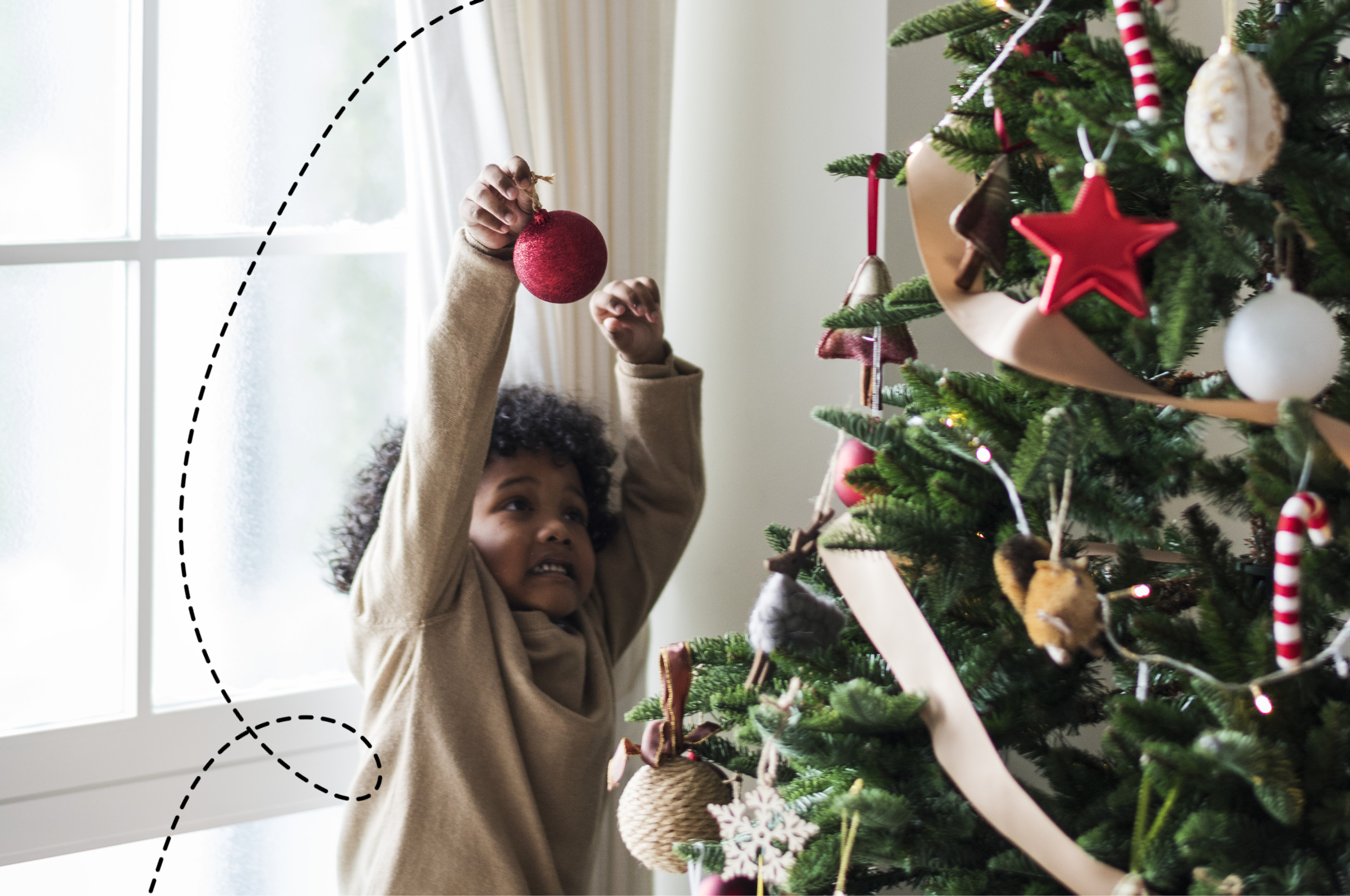 A photo of a little boy holding a bauble up to a Christmas tree
