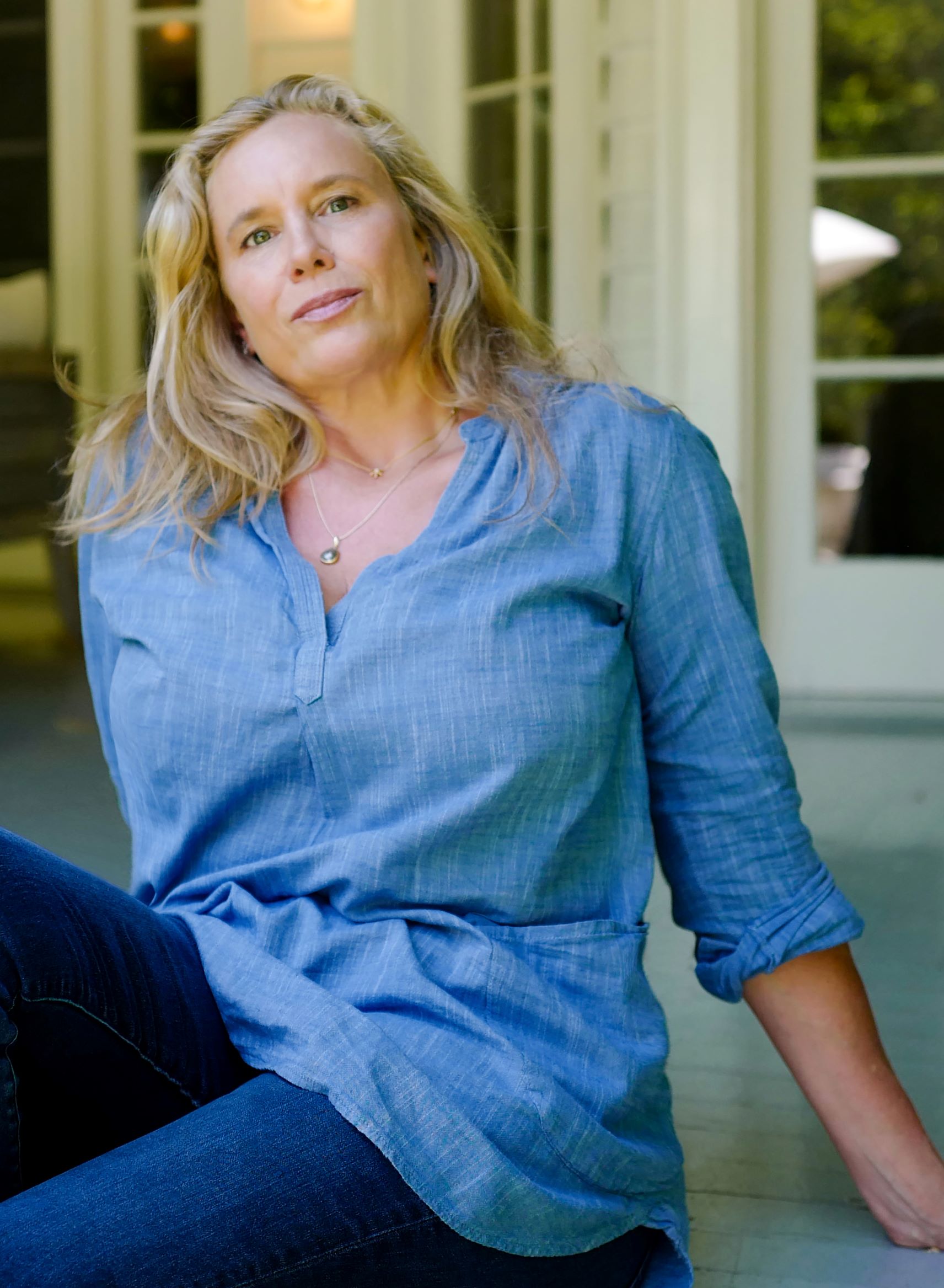 Miranda Cowley Heller sitting back on her hands, wearing a light blue denim shirt and looking at the camera.