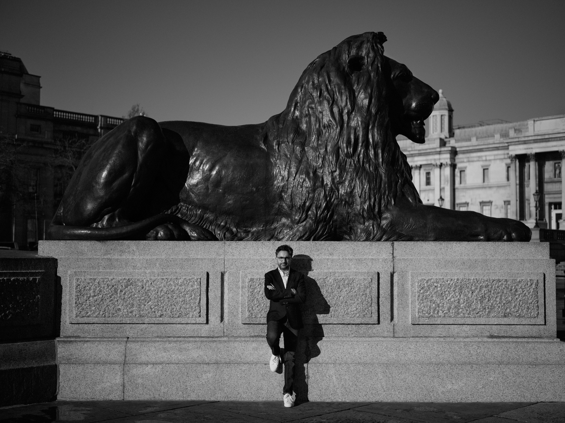 Black and white photograph of Sathnam Saghera, leaning against a statue of a lion.
