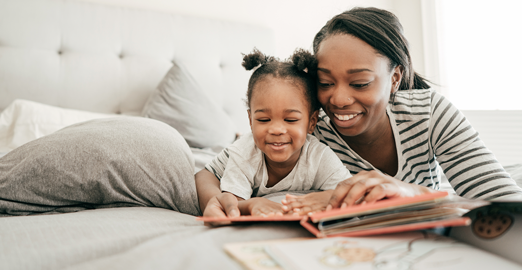 A photo of a mother and young daughter laying on a bed and reading a bedtime story together