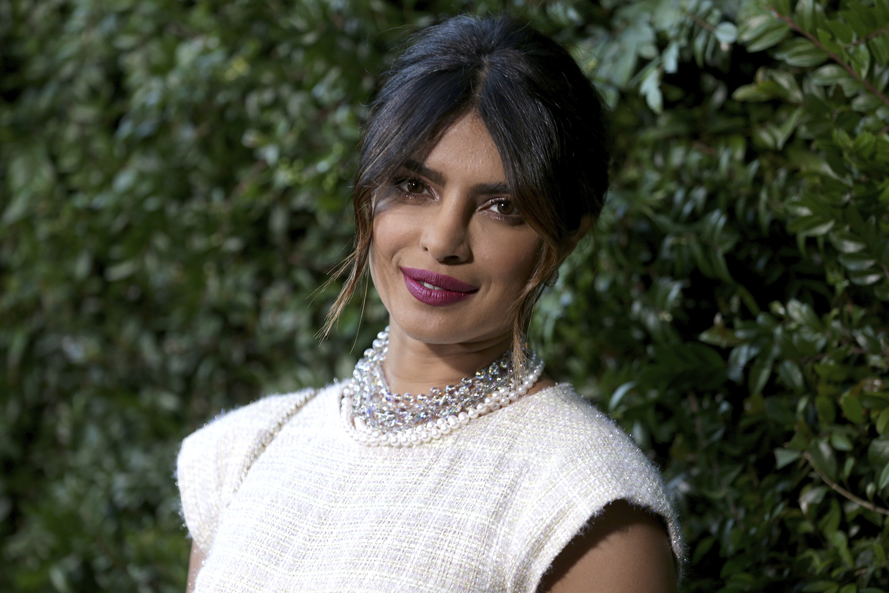 Photograph of Priyanka Chopra wearing a white dress, with her hair up, looking at the camera. Image: Rich Fury/Getty Images