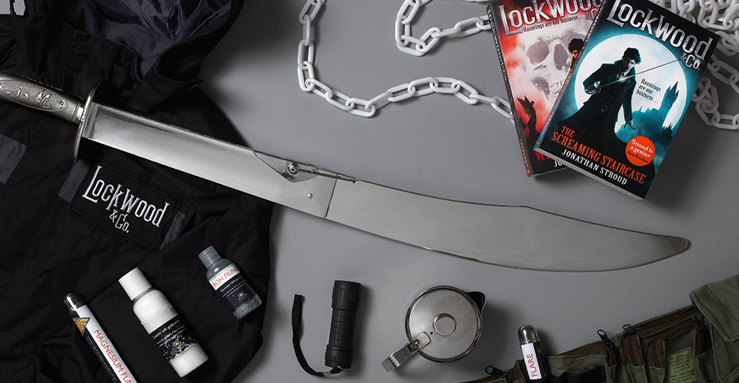 A photo of a couple of the Lockwood books on a grey background next to a fake sword, torch, teapot and coat