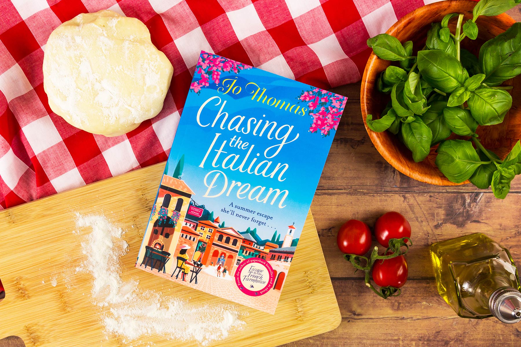 The book Chasing the Italian Dream on an Italian-style table with tomatoes, basil and more.