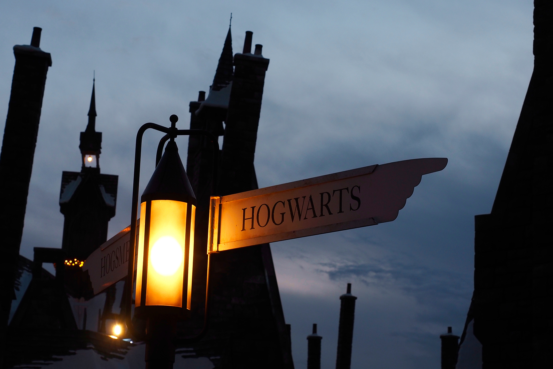 A photo of some buildings in silhouette against a dusky blue sky with a sign saying 'Hogwarts' next to a lamp