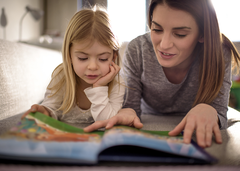 A photo of a mother and her daughter laying on the ground whilst reading a book together