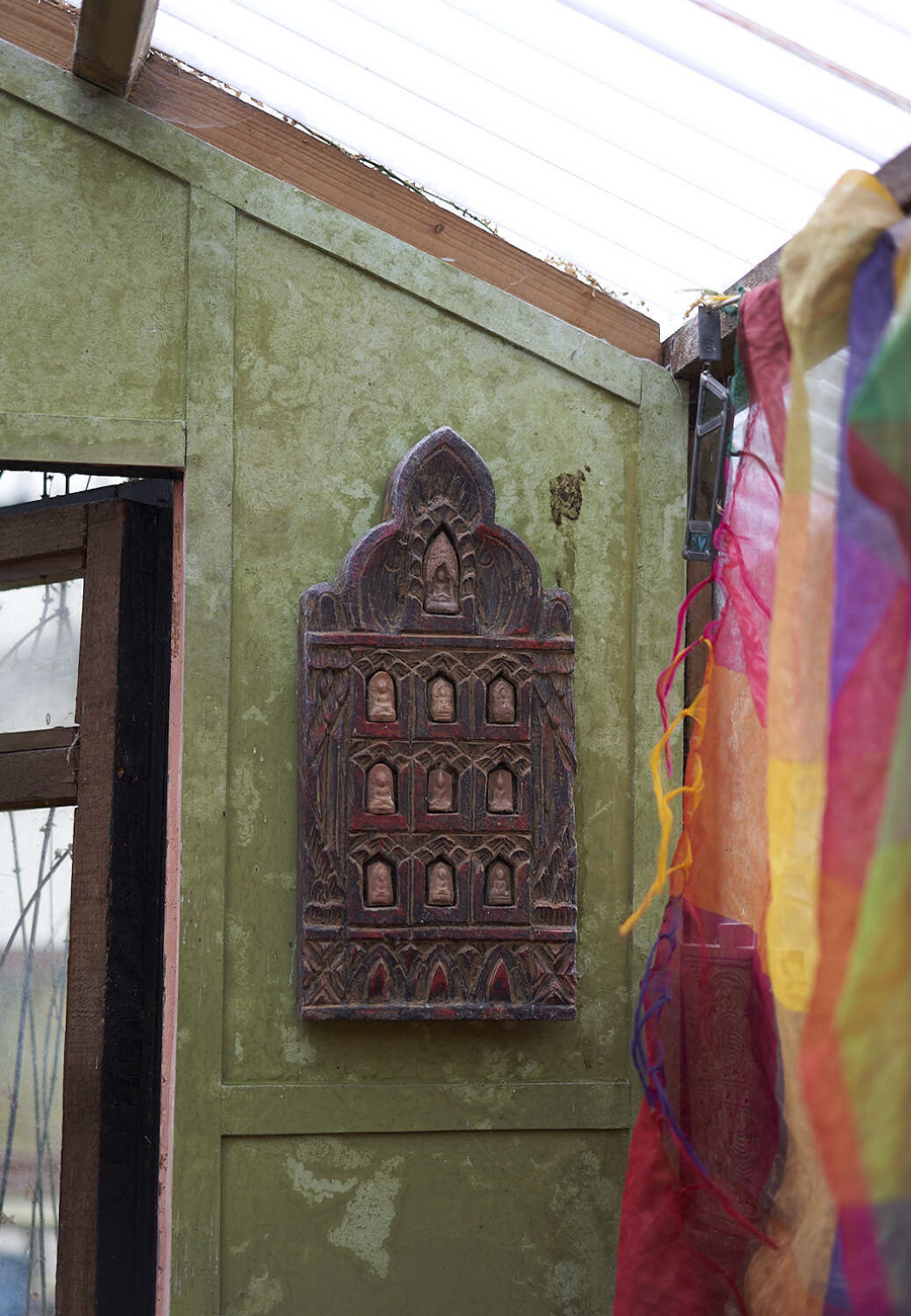 A photograph of a green wall, with a wooden ornament, next to a rainbow curtain.