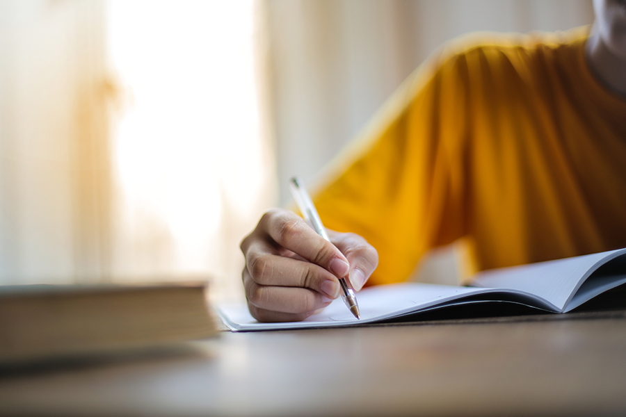 A close up photo of a young persons hand, holding a pen as they write in a notebook