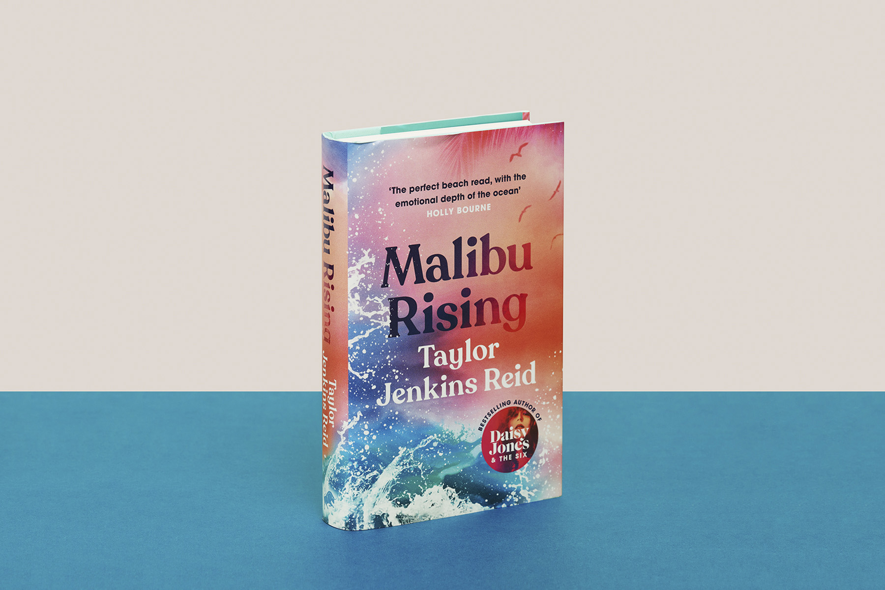 A photograph of a copy of Malibu Rising against a blue and cream backdrop