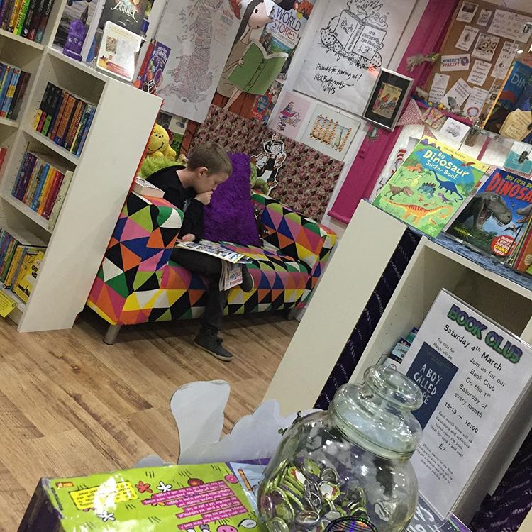 A photo of the inside of the Chicken & Frog Bookshop - there is a young boy sitting on a raindow sofa reading a book