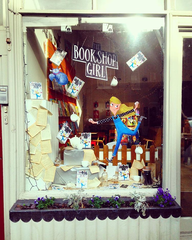 A photo of the outside of the shop Pickled Pepper Books - there is a cartoon cut out of a girl in the window alongside a selection of books