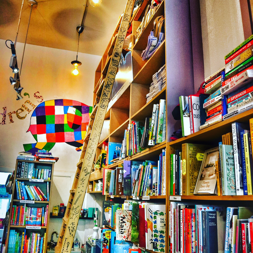 A photo of the inside of The Edinburgh Bookshop, there is a big mural of Elmer the elephant on the back wall