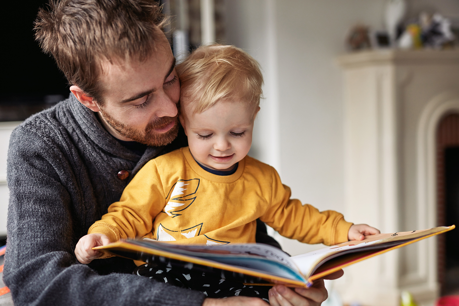 A photo of a father with his son sitting in his lap reading a book together