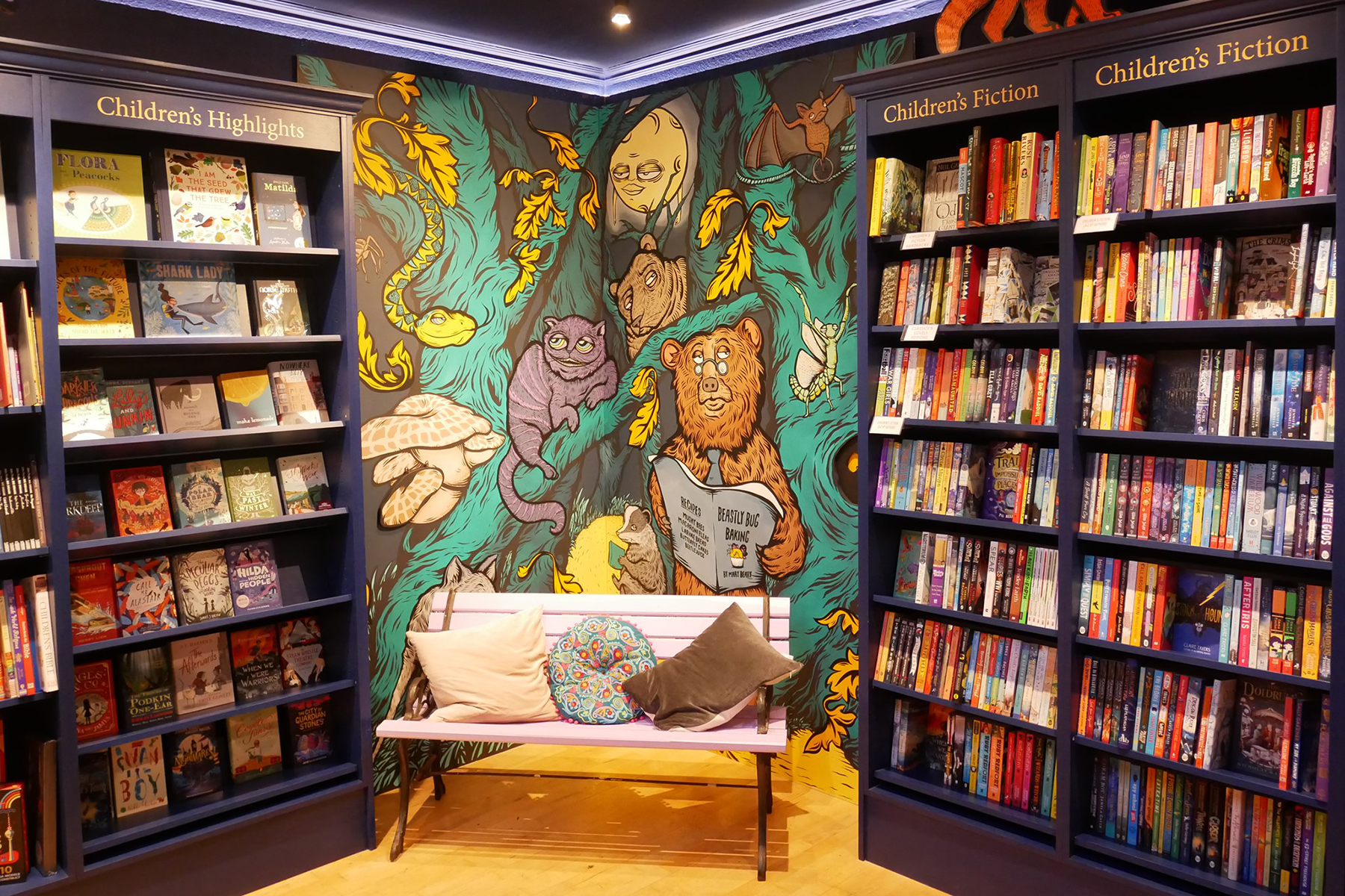A photo of the inside of Mr B’s Emporium of Reading Delights - there is a colourful mural in the corner featuring a cat, two bears, a bat and the moon 