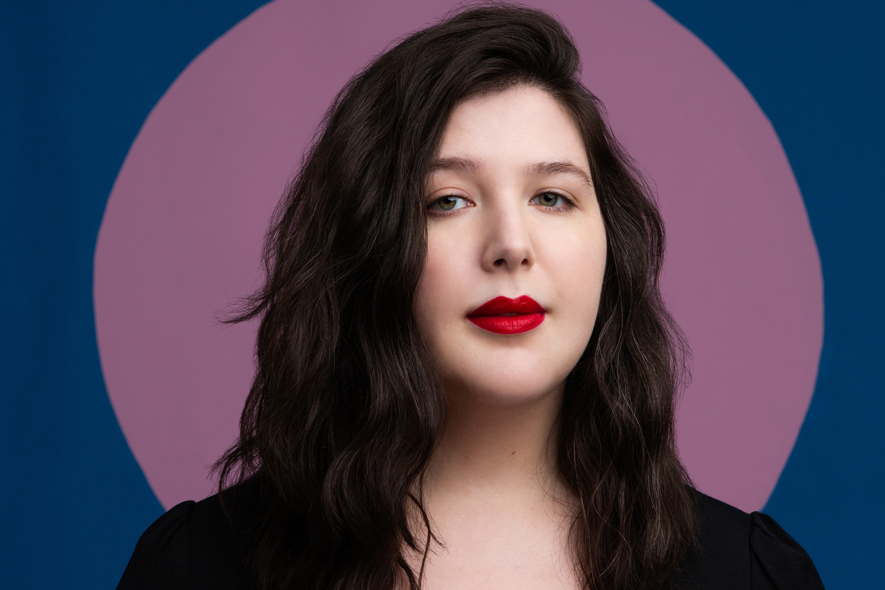 A photograph of Lucy Dacus against a pink and blue backdrop