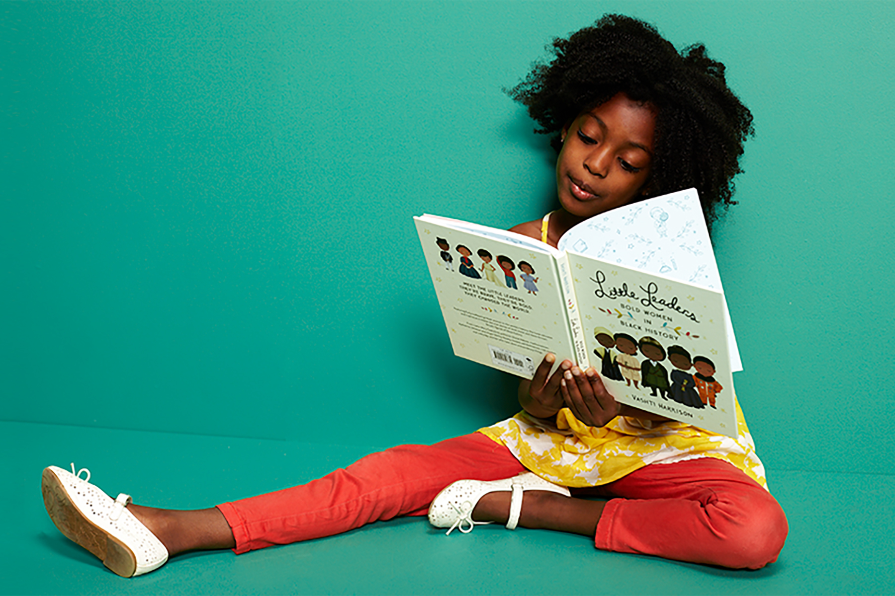 A photo of a young girl against a green background sitting down and reading a book