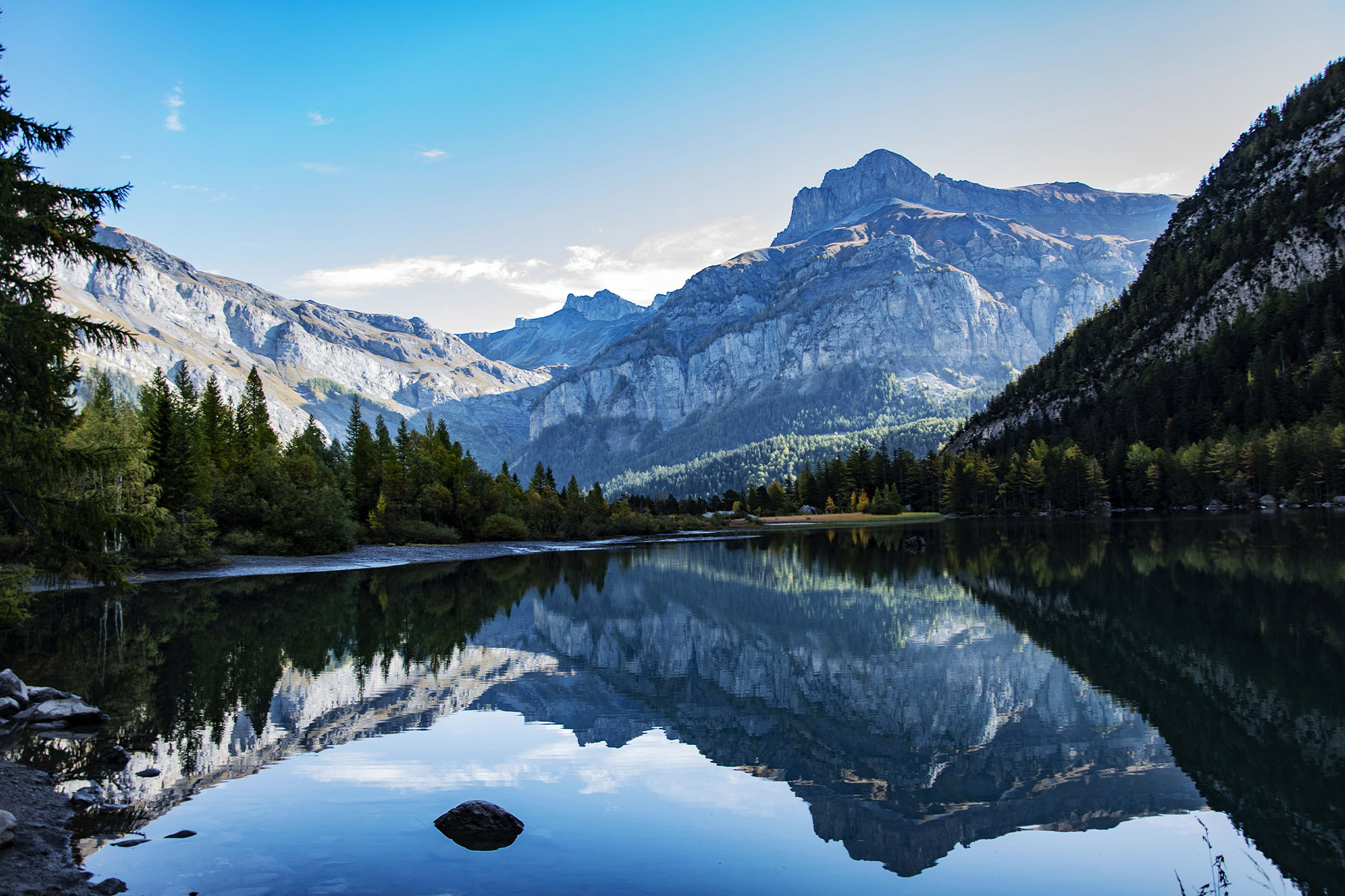 A photo of the spectacular Swiss Alps reflected in a body of water, with trees on either side.
