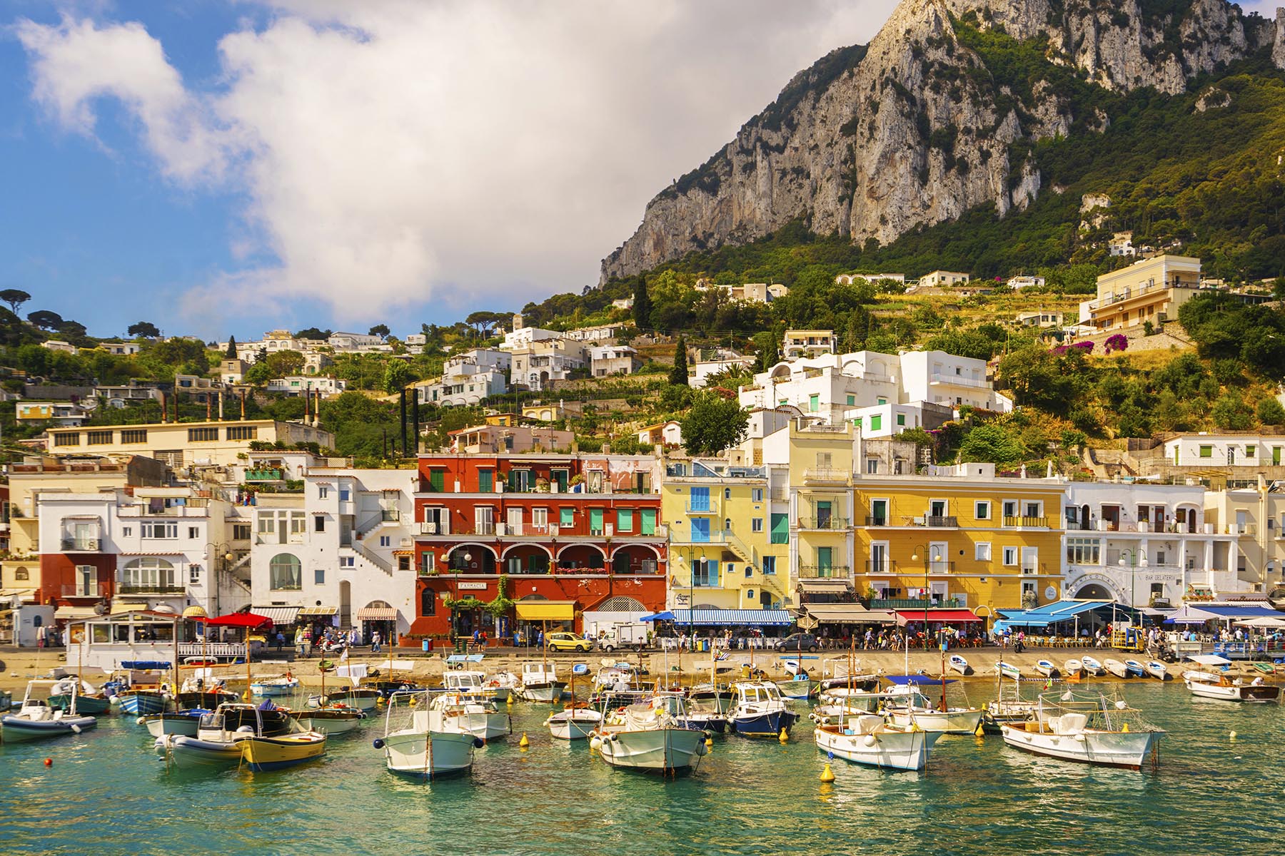 A photo of vividly hued houses on the shore of Capri, with boats anchored in the water out front.