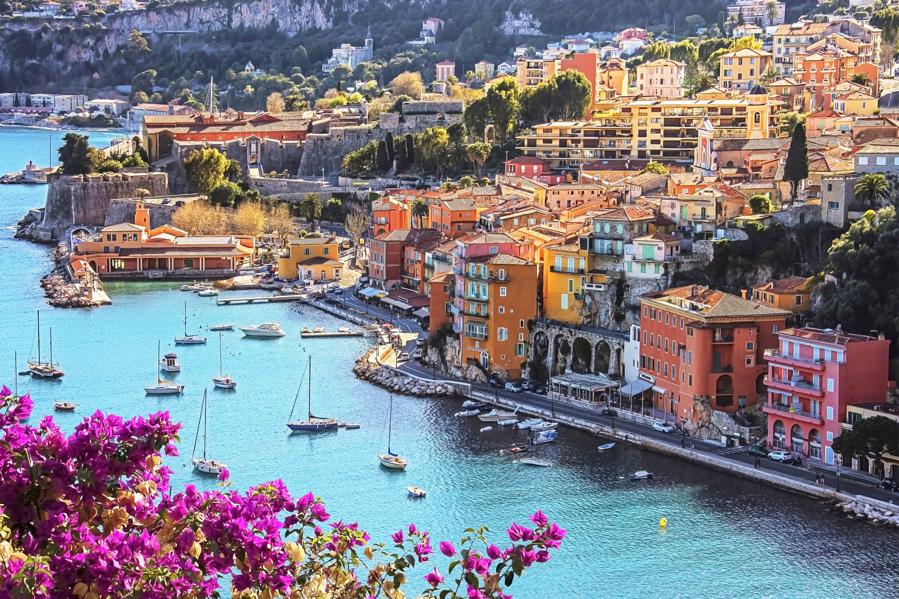 A photo of colourful houses along the French Riviera, with boats floating along the bank.