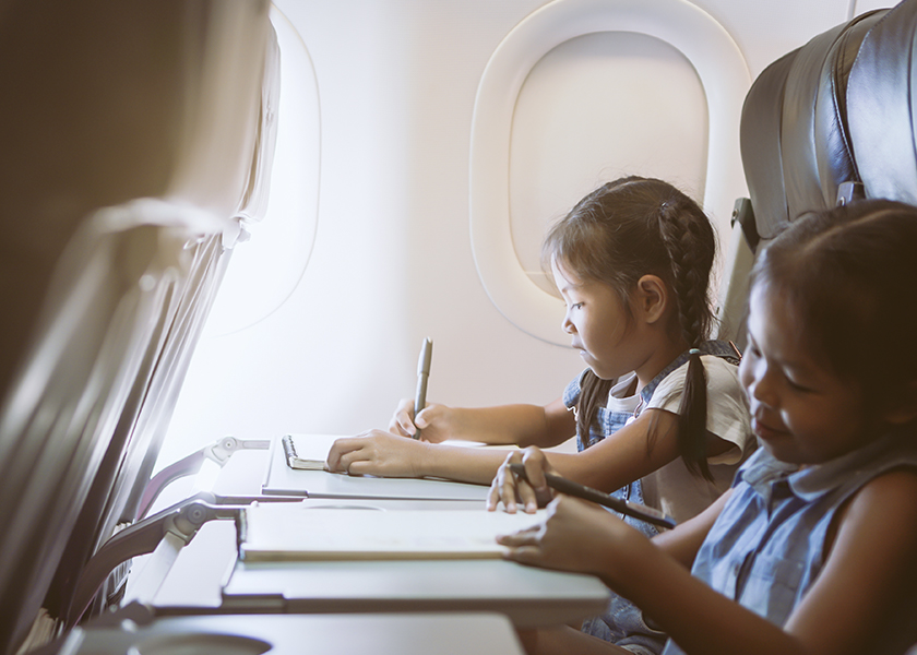 A photo of two little girls sitting on an airplane whilst they write and draw on a notepad