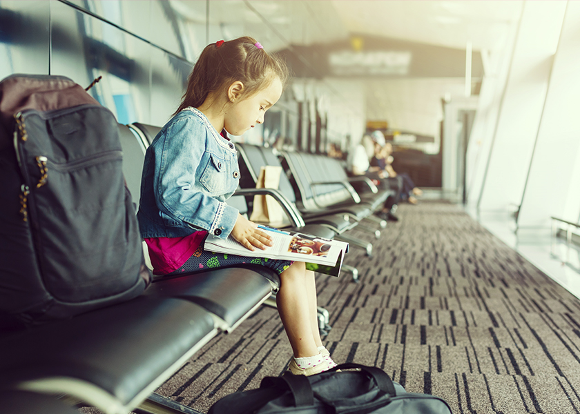 A photo of a little girl sitting in an airport reading a book