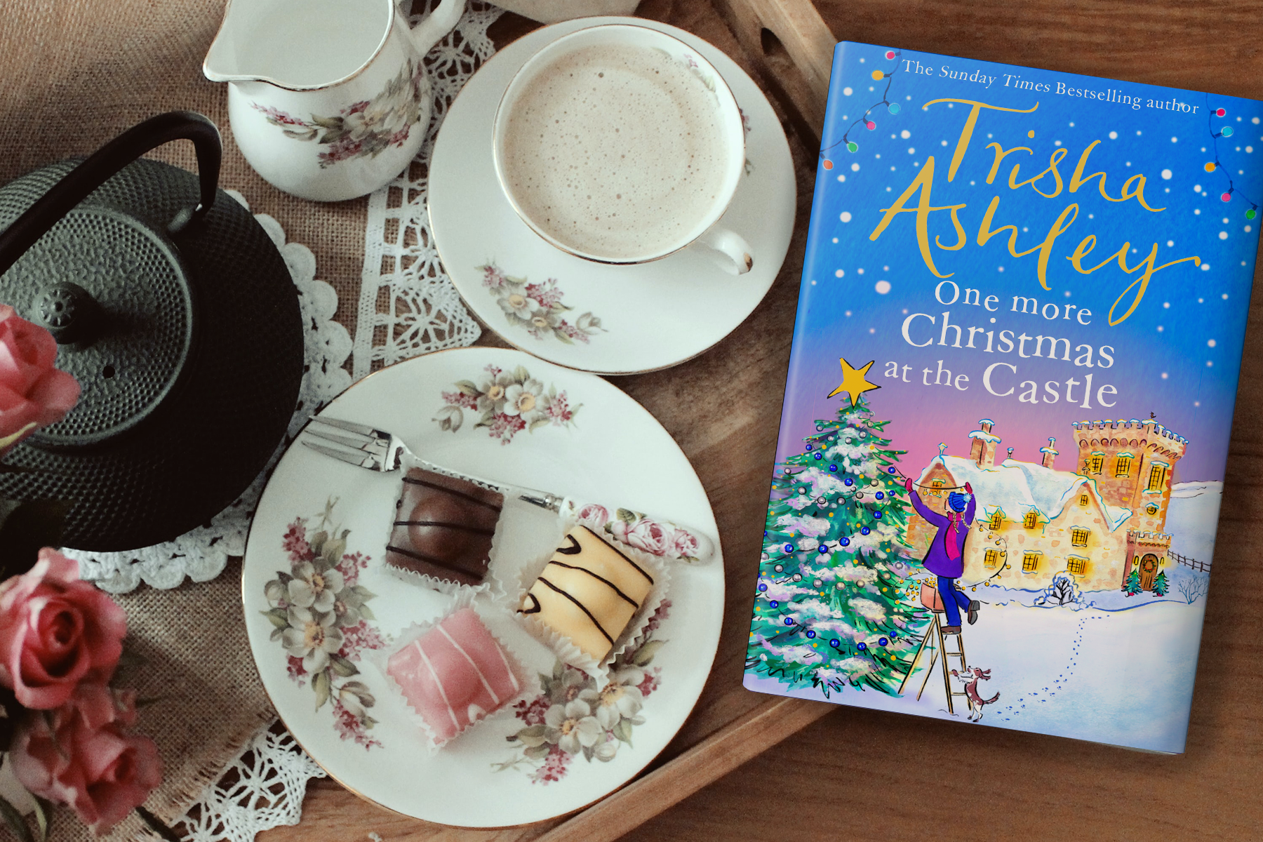 The book One More Christmas at the Castle by Trisha Ashley on a table spread with chocolates, tea and more