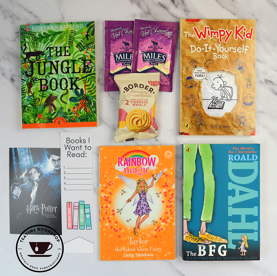 A photo of a selection of books included in the Tea Time Bookshop subscription; it features a few Pufifn books as well as some snacks and a bookmark on a marble background