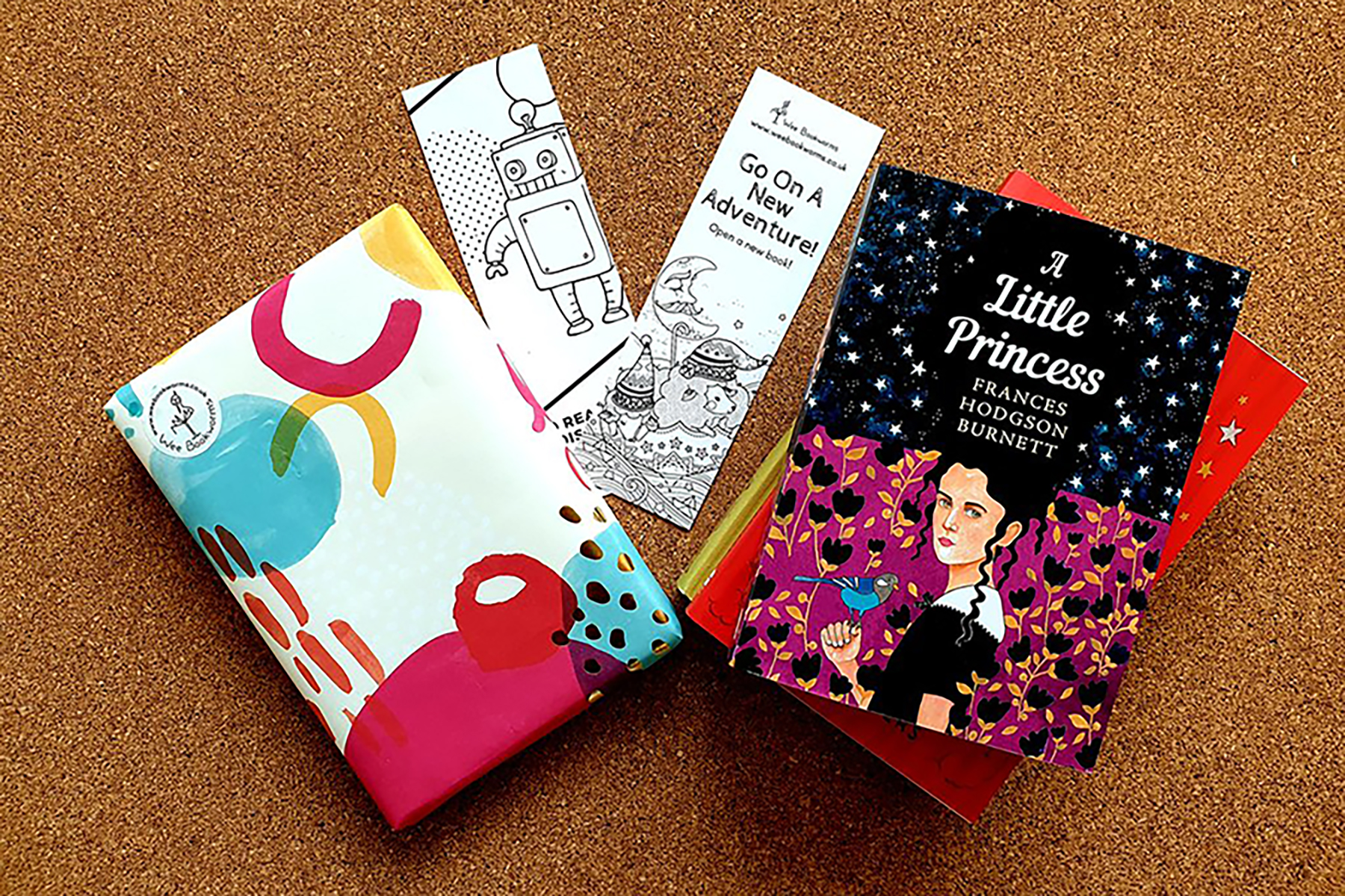 A photo of one of Wee Bookworms subscription boxes; it includes a Puffin edition of A Little Princess next to a gift wrapped book and a couple of paper bookmarks on a wooden background
