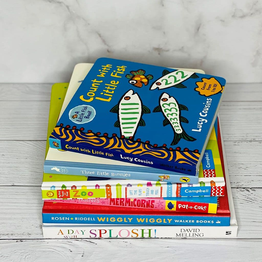 A photo of a stack of children's books all piled up on top of each other; they are on a wooden floor and against a marble backdrop