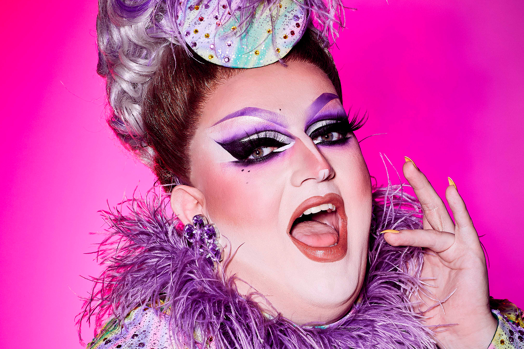 A photo of Drag Race superstar Lawrence Chaney, in hues of purple against a pink background.