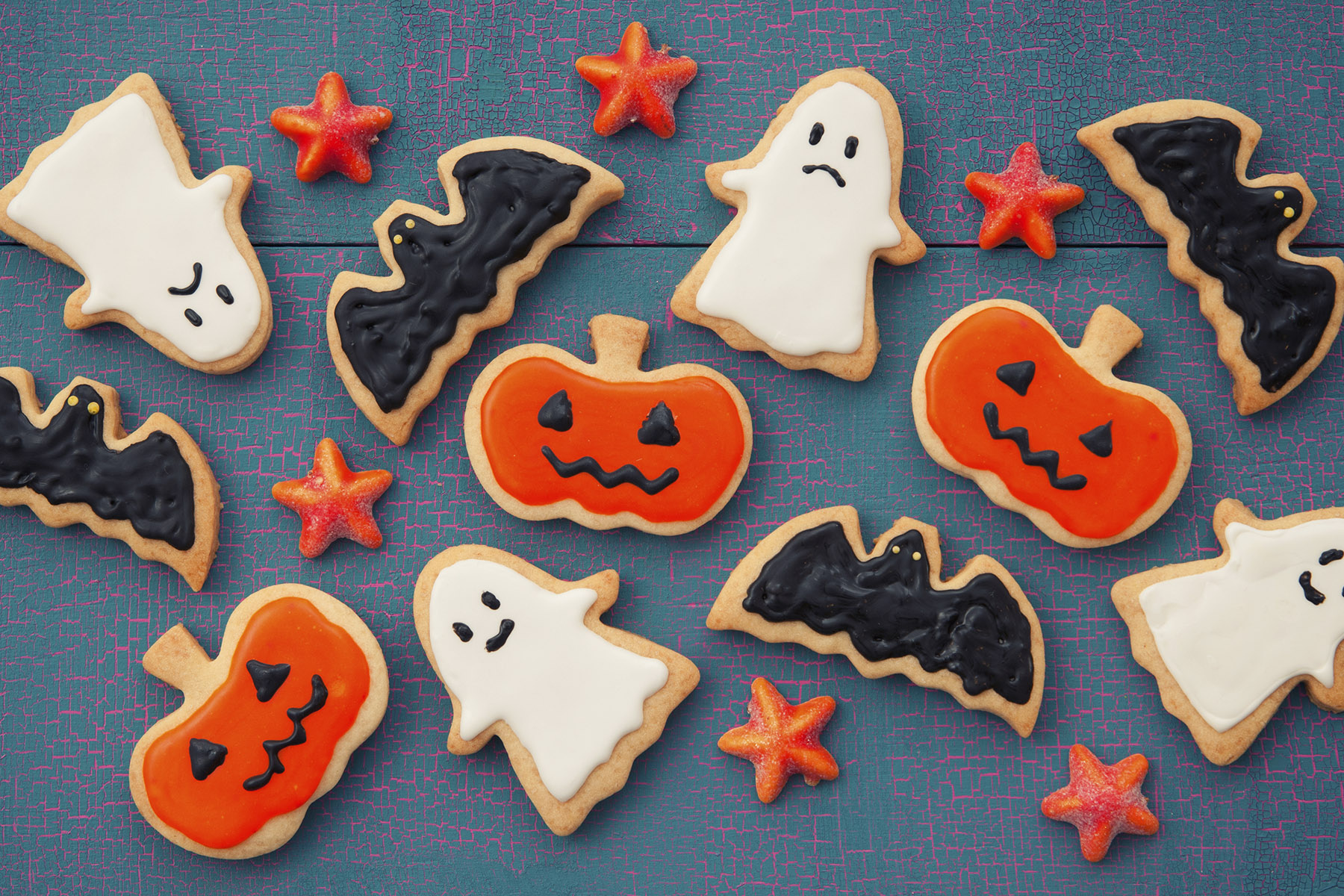A picture of iced Halloween-themed biscuits on a blue background. There are ghost, bast, pumpkin and star biscuits
