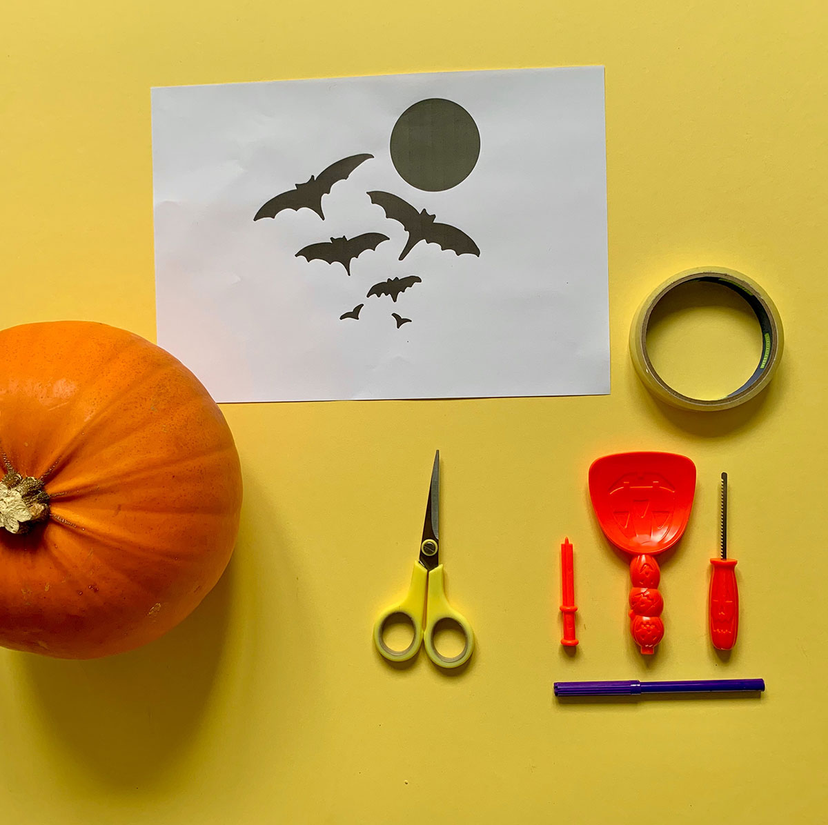 A photo with all the materials you will need for pumpkin carving including a pumpkin, stencil print out, scissors, sticky tape, a scoop, a poker, small serrated knife, and coloured pen