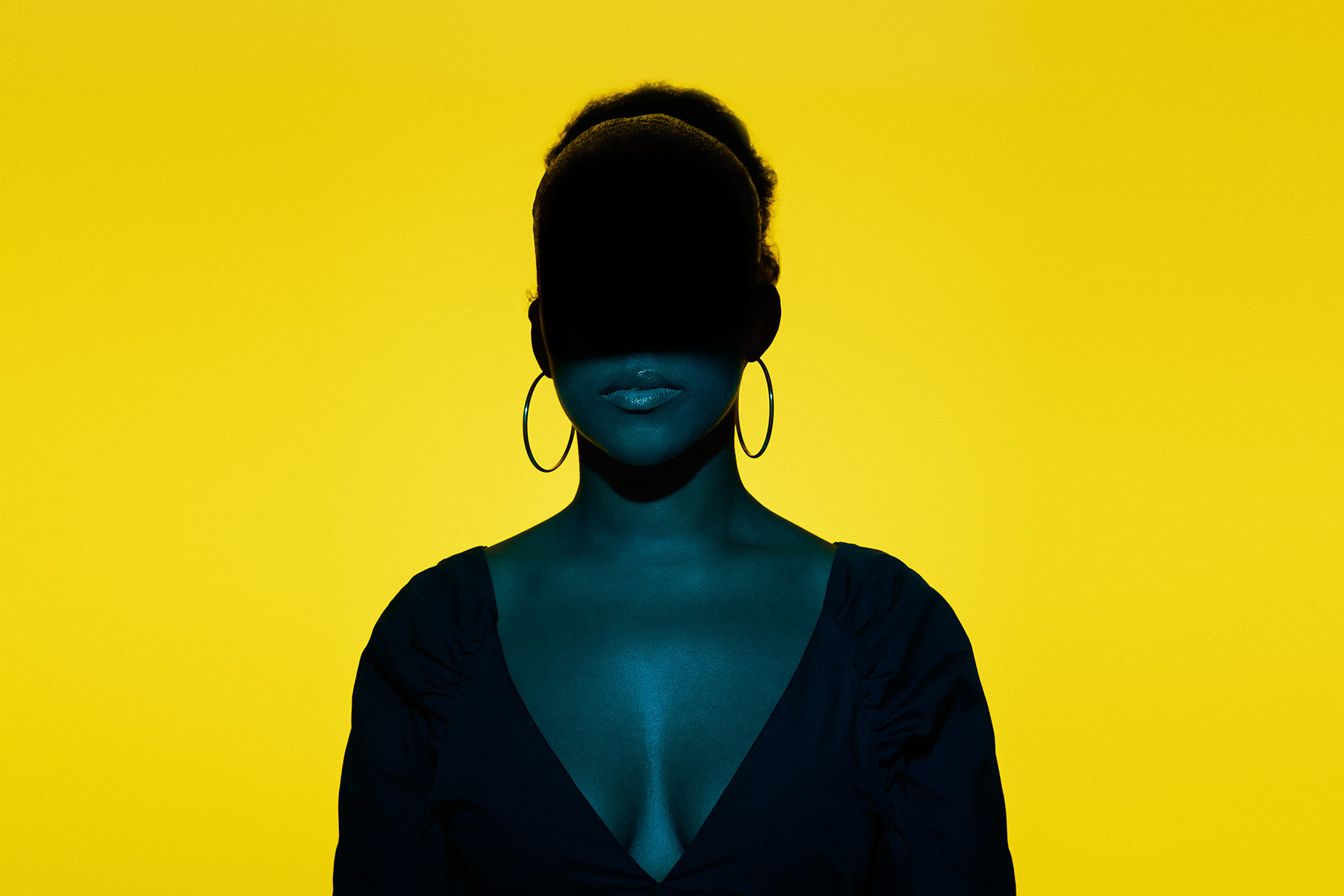 A photo of Jade LB, the anonymous author of Keisha the Sket, with the upper half of her face in shadows, shot against a yellow background.
