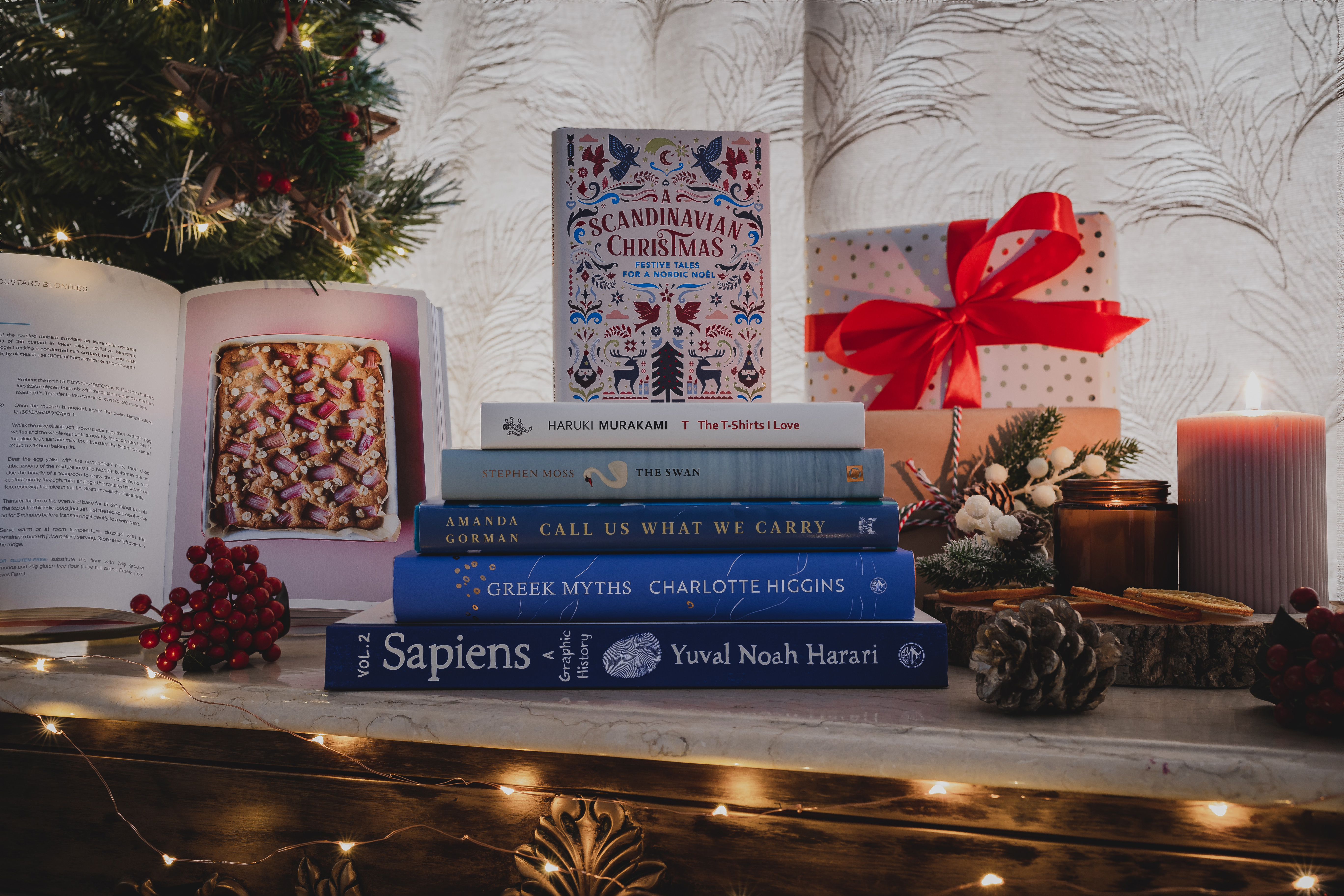 A stack of books with one propped up and open to the side, with Christmas decorations around them all. 