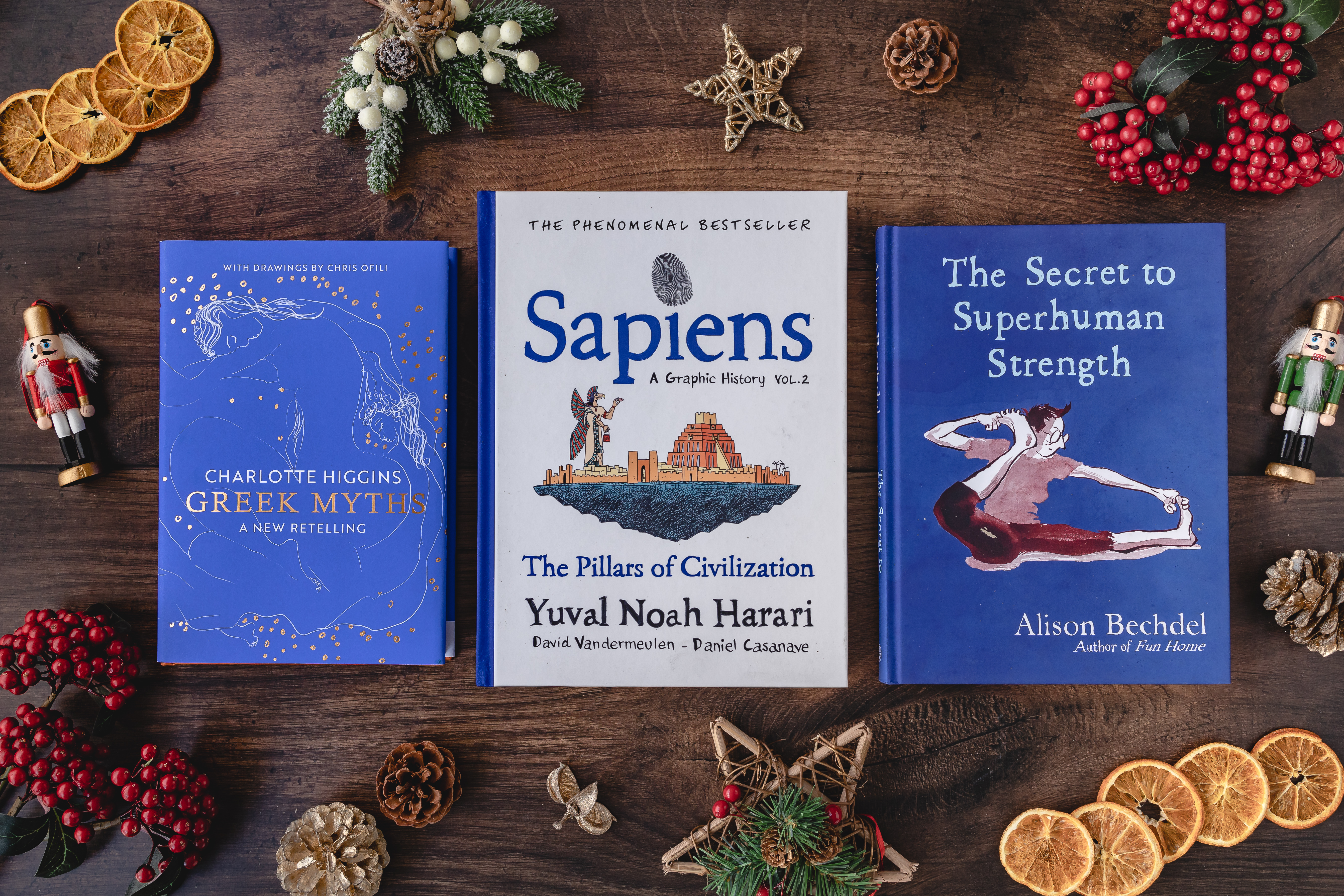 Aerial image of Greek Myths, Sapiens and The Secret to Superhuman Strength laid out on a wooden table surrounded by natural Christmas decorations.