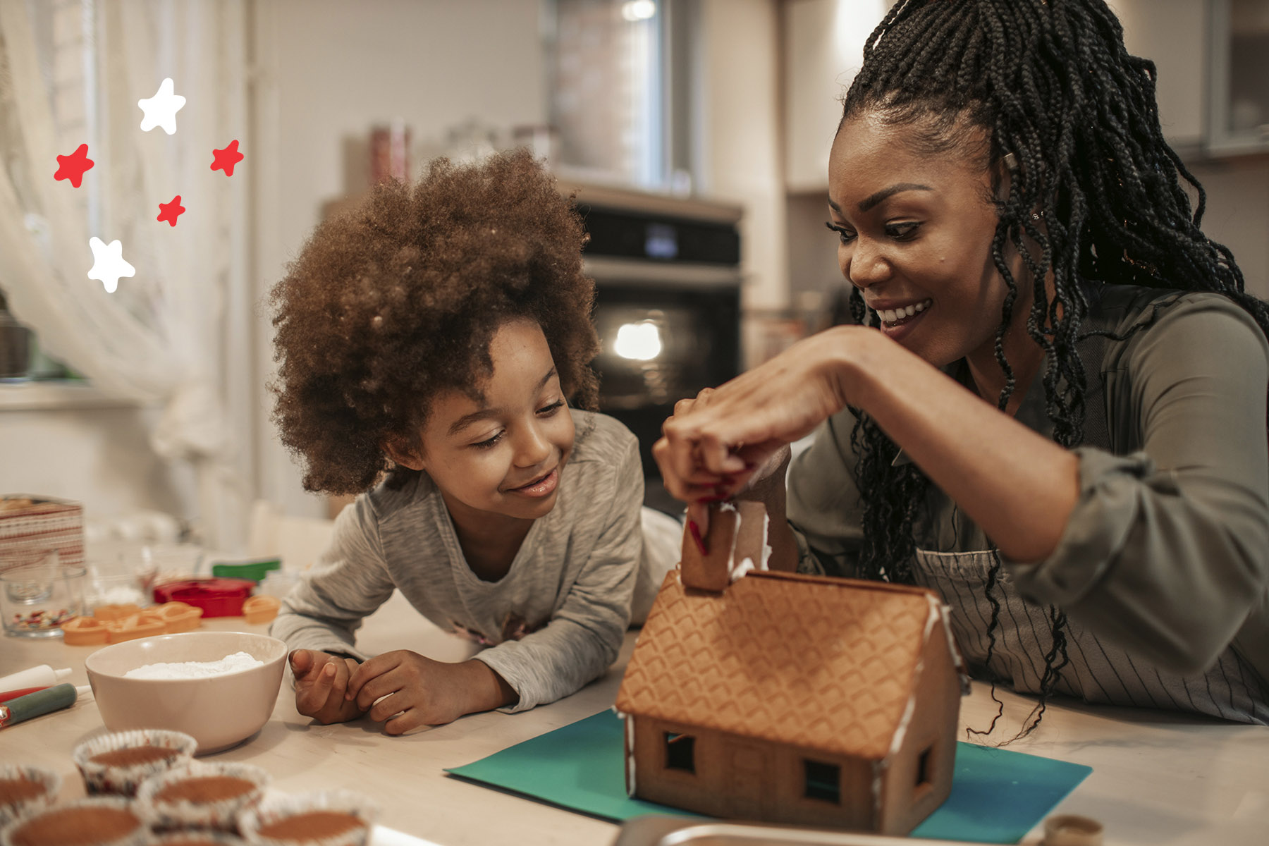 A photo of a little girl and her mum making a gingerbread house together for Christmas