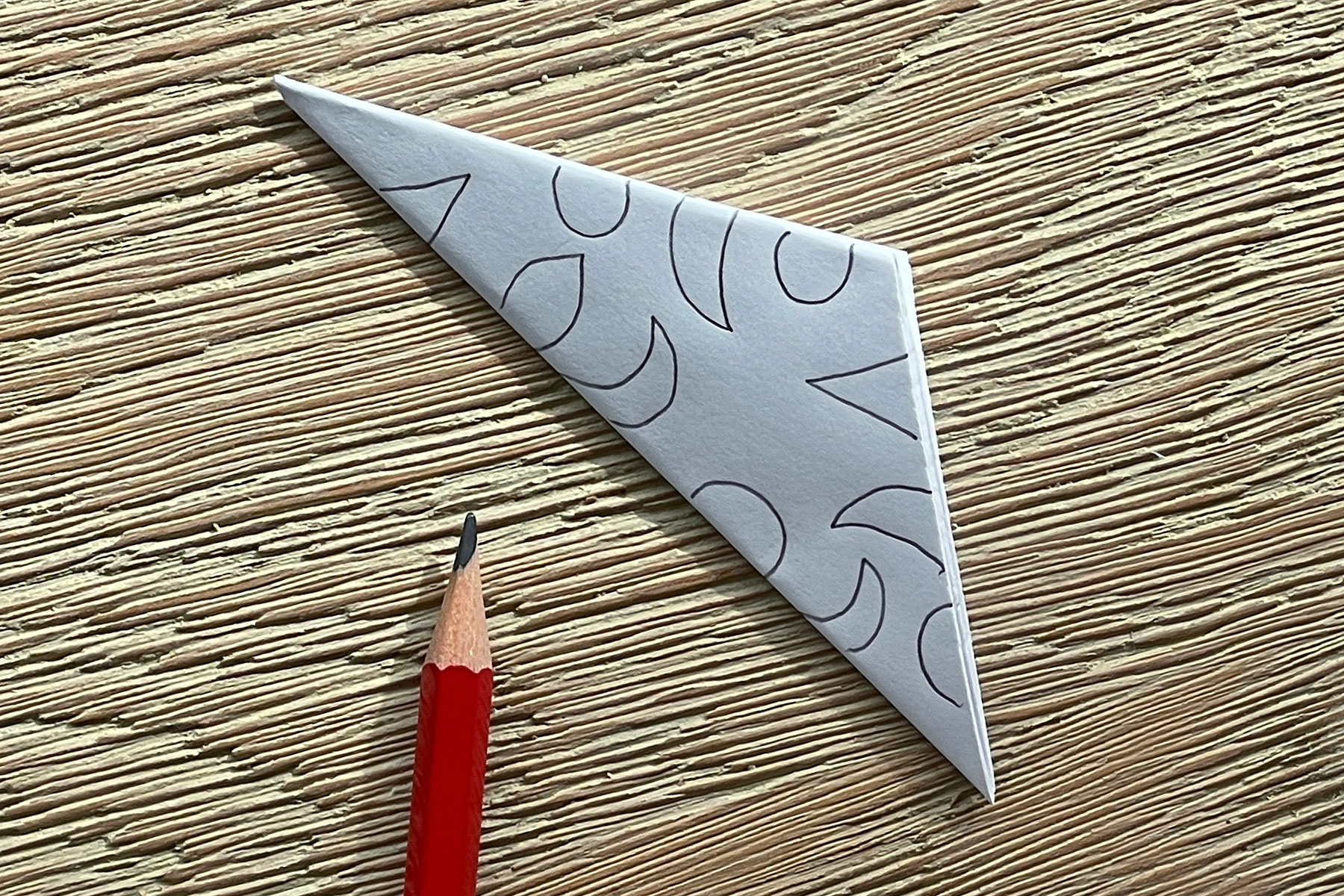 A photo of the triangle piece of paper with shapes drawn on it with a pencil