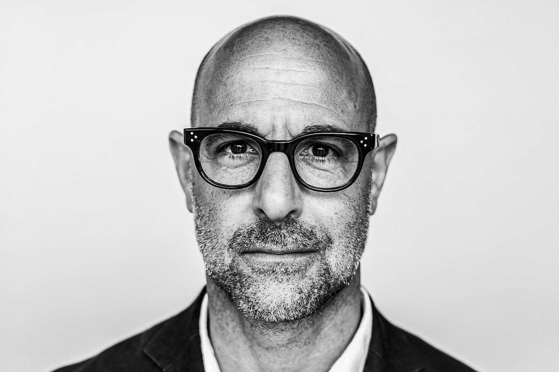 A black and white photograph of Stanley Tucci's head and shoulders.