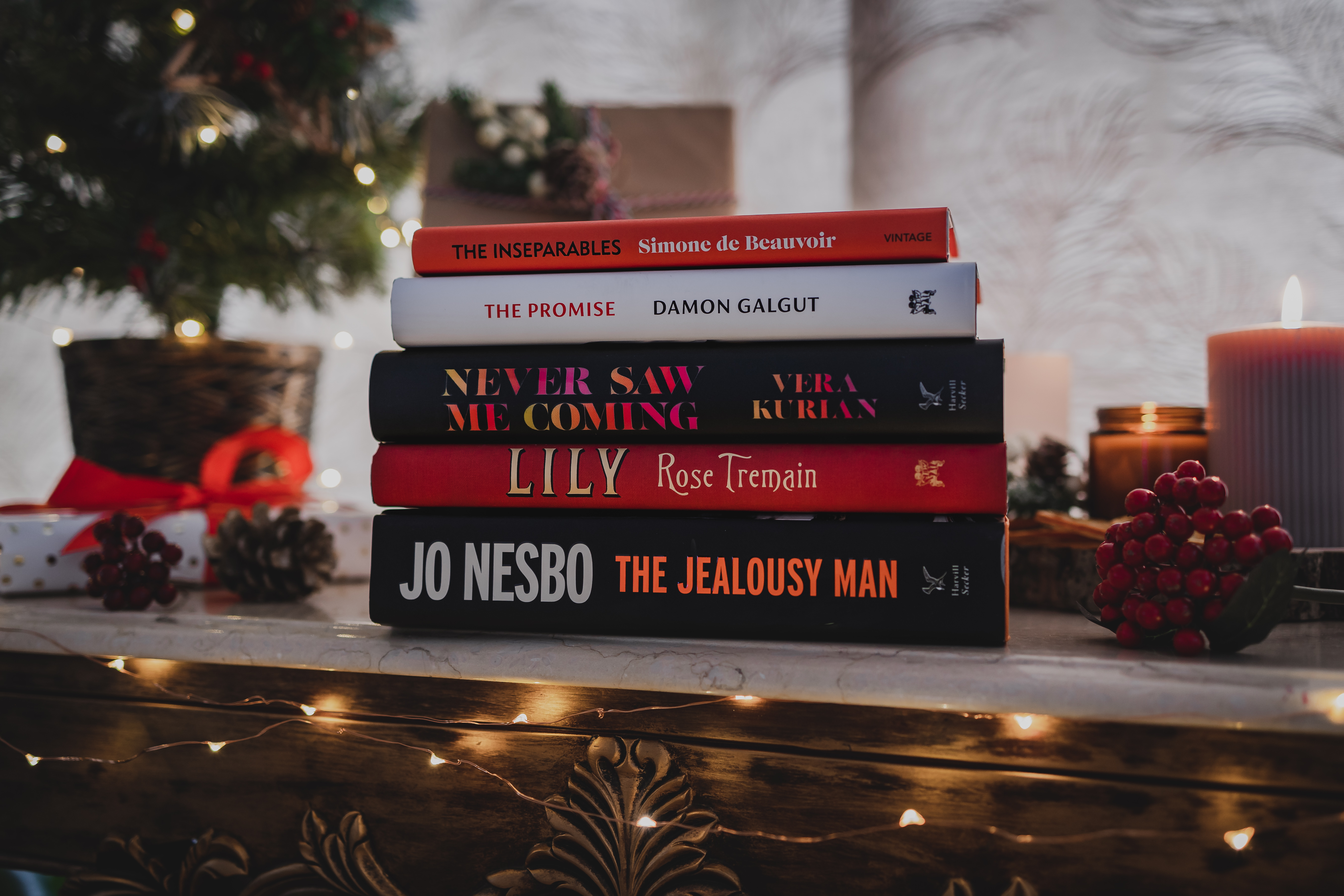 Pile of books on a shelf with Christmas decorations in the background.