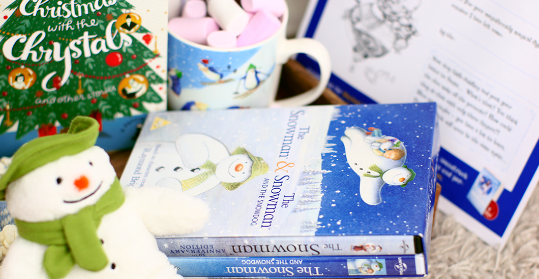 A photo of a copy of The Snowman DVD, Christmas with the Chrystals book, marshmallows in a penguin mug, and a snowman plushie toy