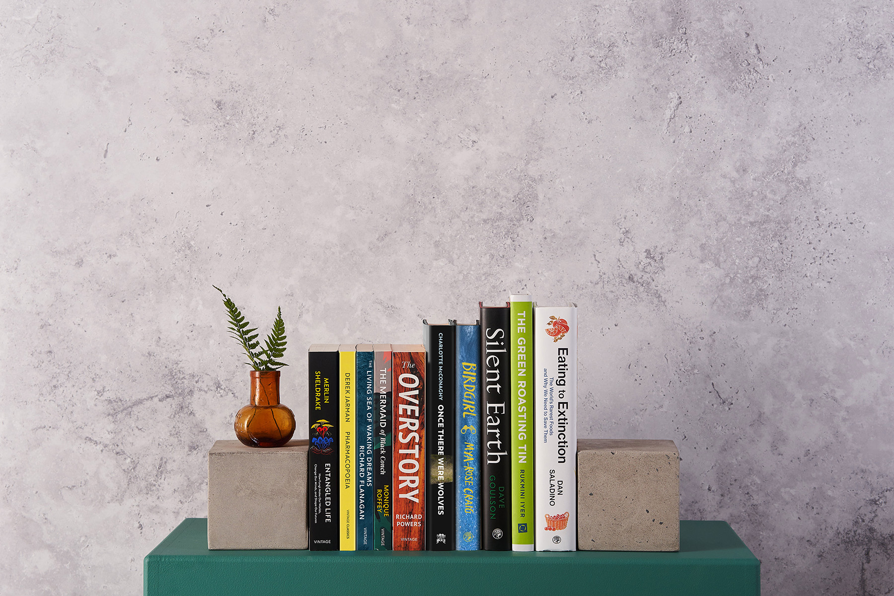Vintage books on nature lined up on a green shelf, spines facing outwards, against a stone background.